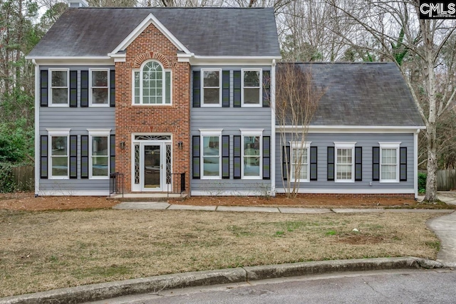 colonial inspired home featuring a shingled roof, brick siding, and a front lawn