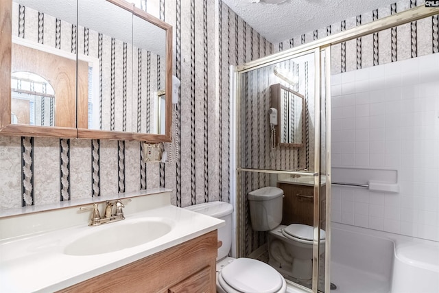 bathroom featuring a textured ceiling, toilet, vanity, a stall shower, and wallpapered walls