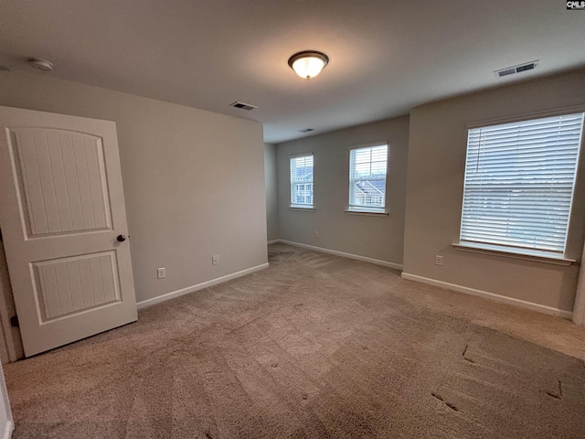 unfurnished room with light colored carpet, visible vents, and baseboards