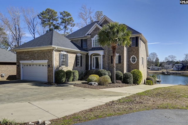 view of front of house with brick siding, a shingled roof, concrete driveway, a water view, and a garage