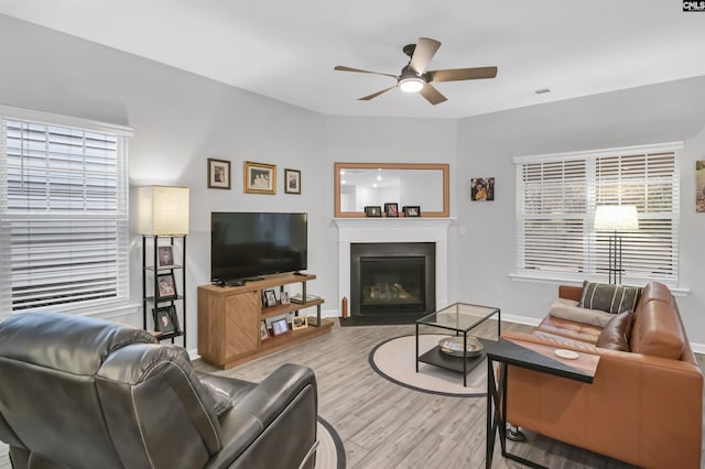 living area featuring visible vents, baseboards, ceiling fan, a fireplace with flush hearth, and light wood-style floors