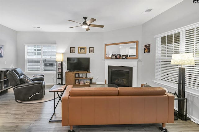 living area with ceiling fan, baseboards, wood finished floors, and a glass covered fireplace