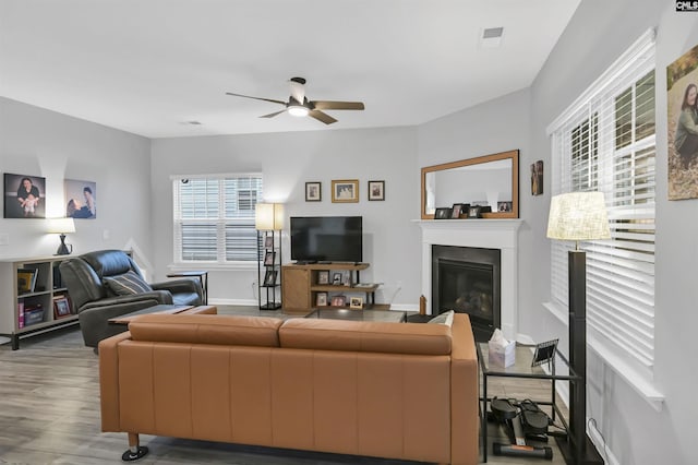 living area with ceiling fan, baseboards, wood finished floors, and a glass covered fireplace