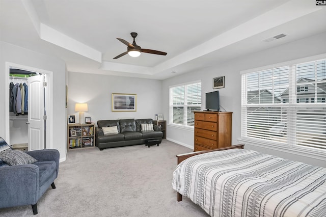 bedroom featuring a raised ceiling, light colored carpet, visible vents, ceiling fan, and baseboards