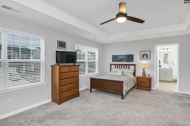 bedroom featuring baseboards, visible vents, a raised ceiling, light colored carpet, and ensuite bathroom