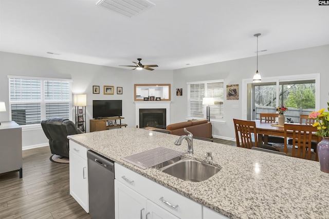 kitchen with open floor plan, decorative light fixtures, stainless steel dishwasher, white cabinetry, and a sink