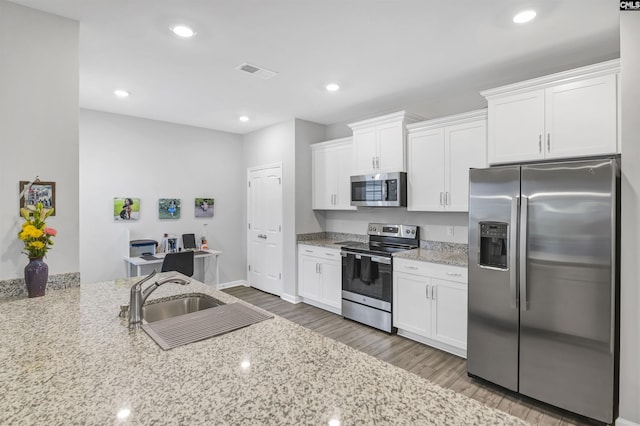 kitchen featuring light stone counters, stainless steel appliances, visible vents, white cabinetry, and wood finished floors