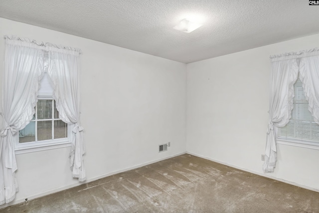 unfurnished room featuring a textured ceiling, a wealth of natural light, carpet, and visible vents