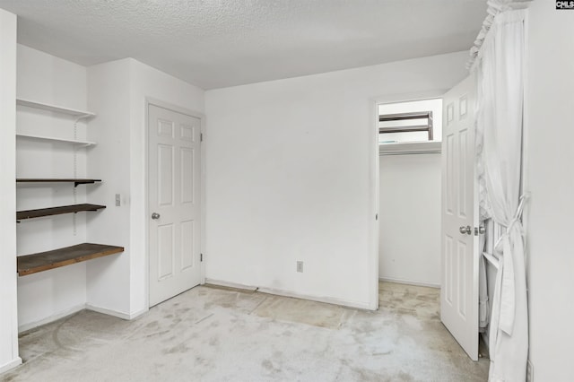 unfurnished bedroom with light carpet, a textured ceiling, a walk in closet, and baseboards