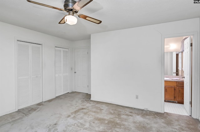 unfurnished bedroom with light carpet, ensuite bathroom, a ceiling fan, and multiple closets