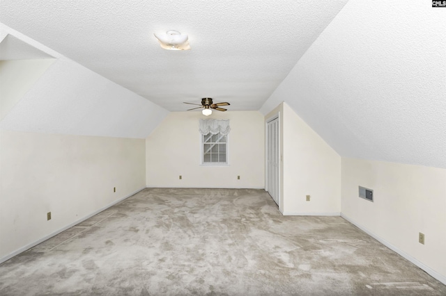 additional living space featuring light carpet, visible vents, lofted ceiling, ceiling fan, and a textured ceiling