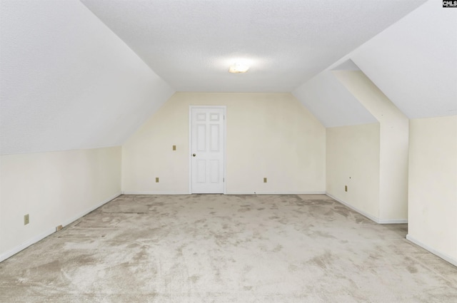 additional living space with light colored carpet, vaulted ceiling, a textured ceiling, and baseboards