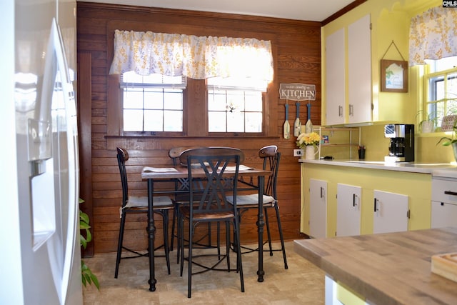 kitchen featuring wooden walls, white refrigerator with ice dispenser, a sink, white cabinets, and light countertops