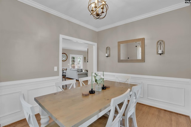 dining area with light wood finished floors, ornamental molding, a notable chandelier, and wainscoting