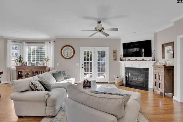 living area featuring baseboards, ceiling fan, ornamental molding, light wood-style floors, and a fireplace