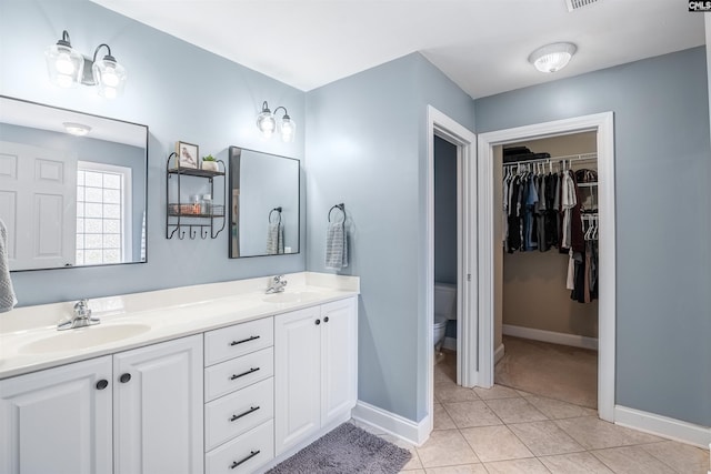 full bathroom with a spacious closet, double vanity, a sink, and toilet