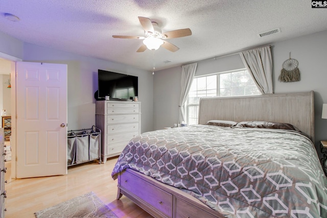 bedroom featuring a ceiling fan, visible vents, a textured ceiling, and light wood finished floors