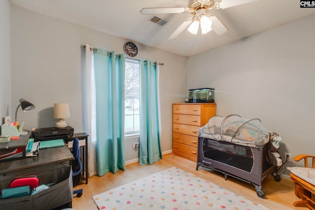 bedroom featuring visible vents, light wood-style flooring, a ceiling fan, a textured ceiling, and baseboards