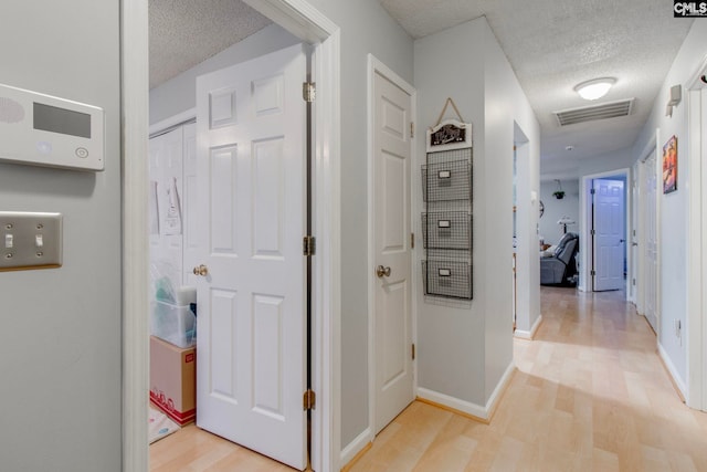 hall with light wood-type flooring, visible vents, a textured ceiling, and baseboards