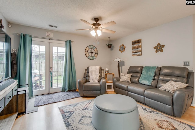 living area featuring light wood-style flooring, visible vents, a textured ceiling, and french doors