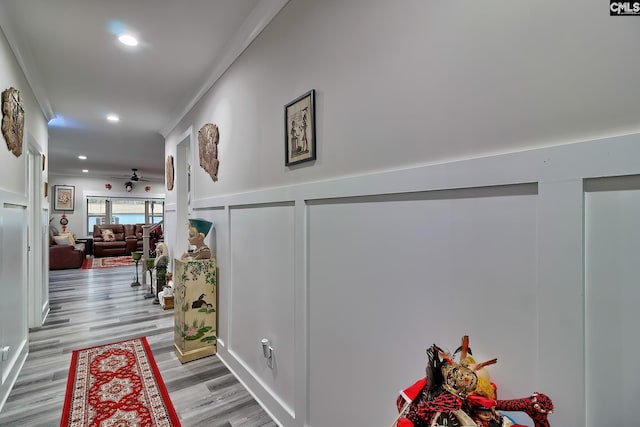 hallway featuring wainscoting, ornamental molding, light wood-type flooring, a decorative wall, and recessed lighting