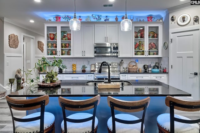 kitchen featuring a breakfast bar, a sink, visible vents, appliances with stainless steel finishes, and glass insert cabinets