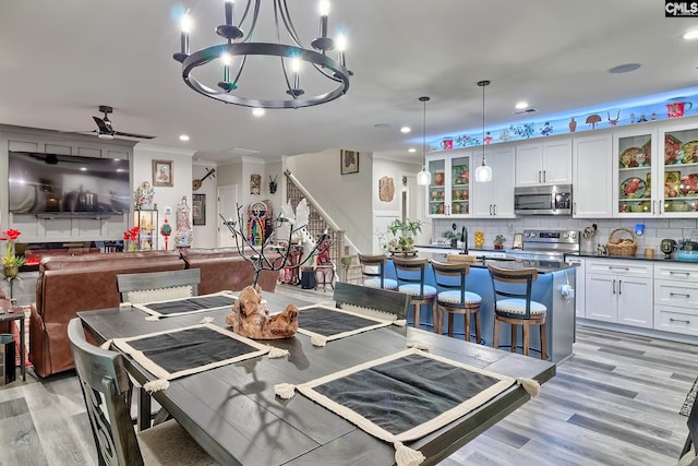 dining area featuring ceiling fan with notable chandelier, stairway, light wood-type flooring, and crown molding