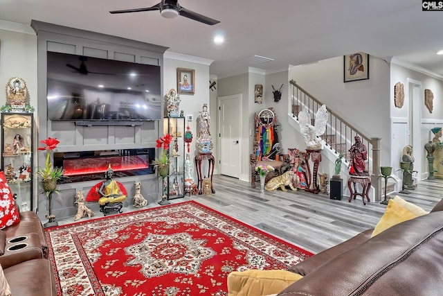 living room with a glass covered fireplace, ceiling fan, ornamental molding, stairs, and light wood-style floors