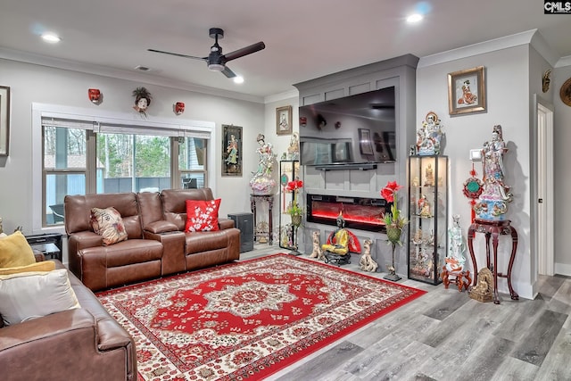 living area with ornamental molding, recessed lighting, a large fireplace, and light wood finished floors