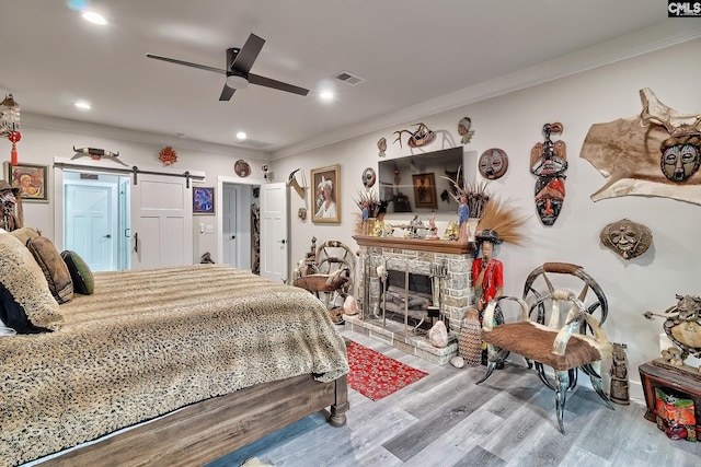 bedroom featuring a barn door, a fireplace, wood finished floors, visible vents, and ornamental molding