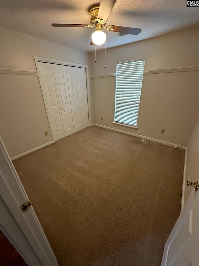 unfurnished bedroom with a textured ceiling, carpet flooring, a ceiling fan, baseboards, and a closet