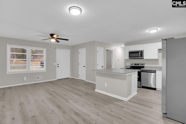 kitchen featuring white cabinets, light stone counters, open floor plan, a center island, and stainless steel appliances