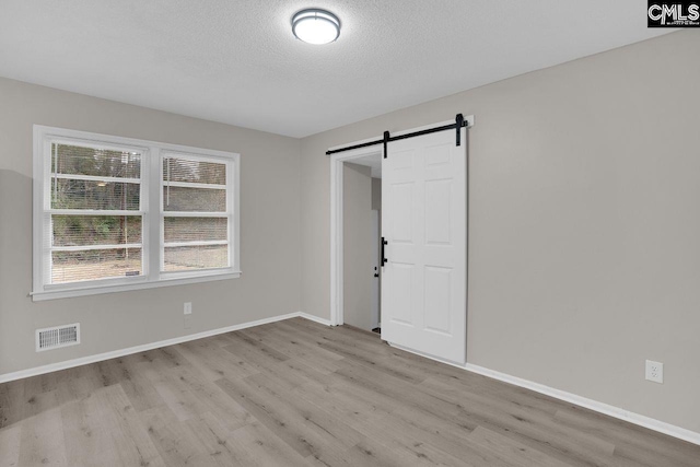 empty room featuring light wood finished floors, a barn door, visible vents, baseboards, and a textured ceiling