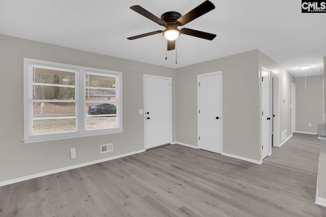 empty room featuring visible vents, light wood-style flooring, attic access, ceiling fan, and baseboards