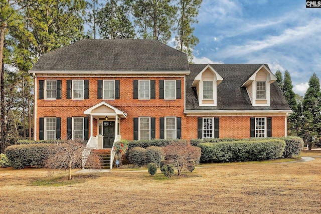 view of front of home featuring roof with shingles, a front lawn, and brick siding