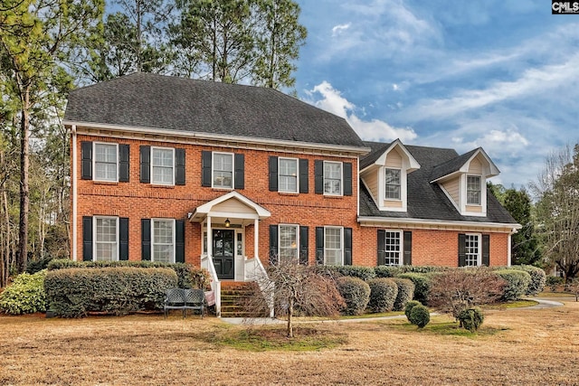 view of front of property with brick siding, a front lawn, and roof with shingles