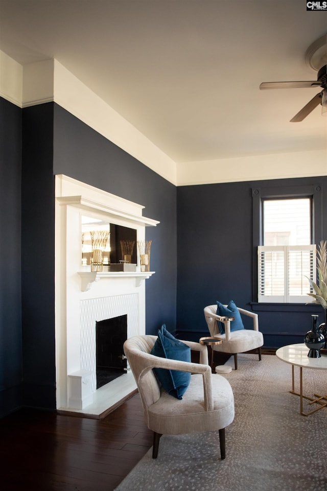 living area featuring a ceiling fan, a fireplace with raised hearth, and wood finished floors