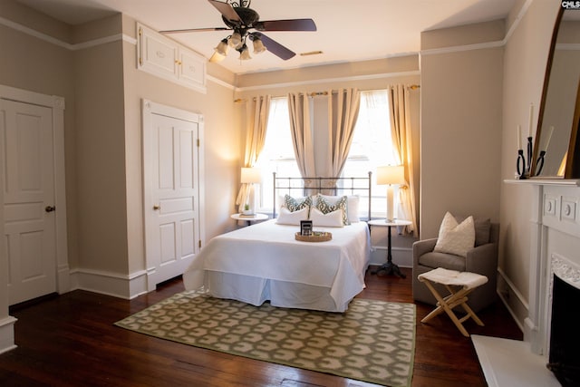 bedroom with a fireplace with raised hearth, ceiling fan, dark wood-type flooring, visible vents, and baseboards