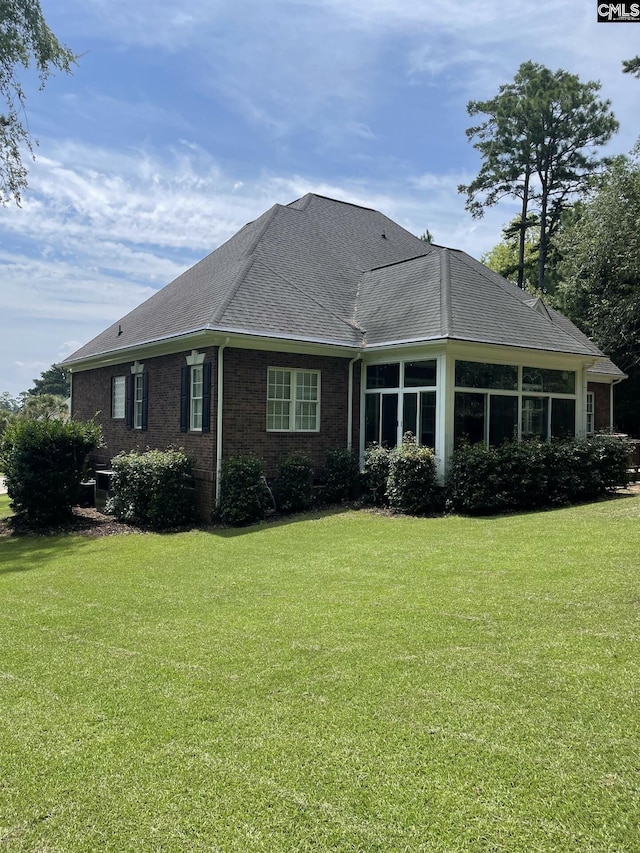 back of property featuring a sunroom, roof with shingles, a lawn, and brick siding