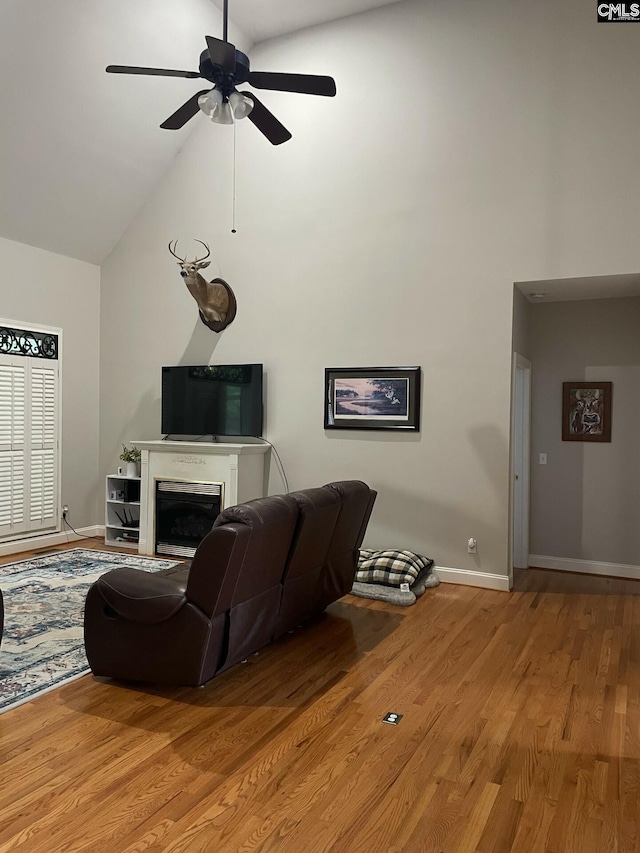 living area with high vaulted ceiling, light wood-type flooring, a fireplace, and baseboards