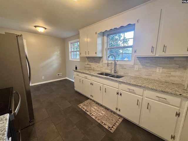 kitchen featuring decorative backsplash, freestanding refrigerator, white cabinets, a sink, and light stone countertops