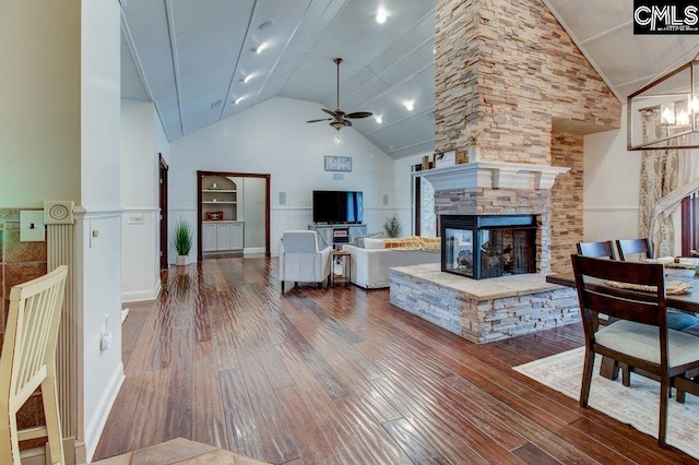 living room with high vaulted ceiling, a fireplace, wood finished floors, a ceiling fan, and wainscoting