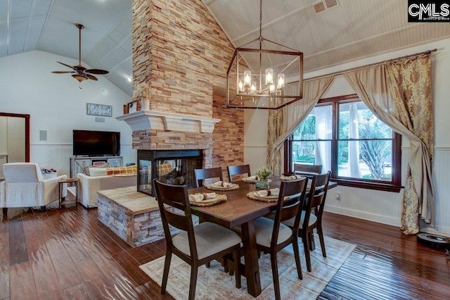 dining area with high vaulted ceiling, ceiling fan with notable chandelier, a fireplace, visible vents, and dark wood finished floors