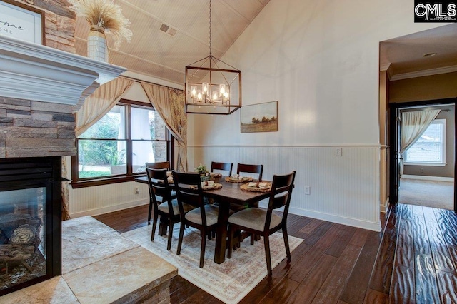 dining area featuring crown molding, a notable chandelier, a fireplace, wainscoting, and wood finished floors