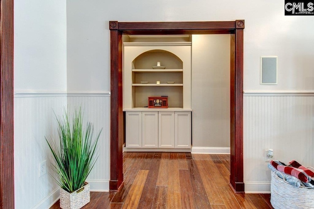 interior space featuring built in shelves, wood finished floors, and wainscoting