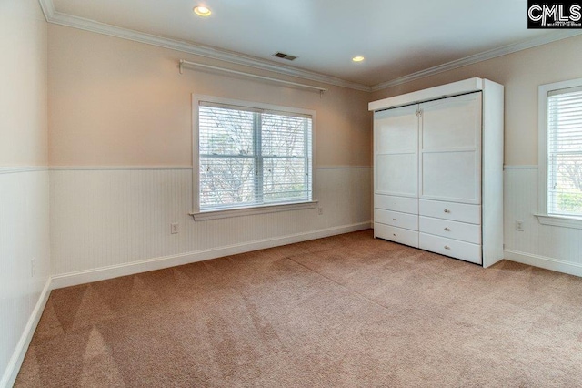 unfurnished bedroom with light carpet, ornamental molding, wainscoting, and visible vents