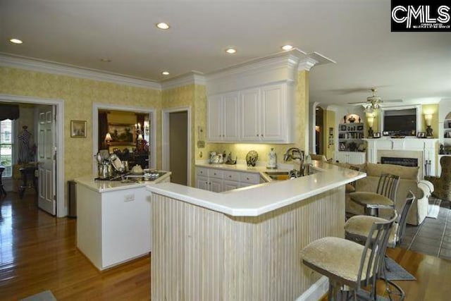 kitchen featuring a breakfast bar area, light countertops, white cabinets, a sink, and a peninsula