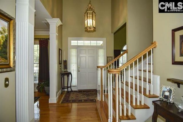 foyer entrance with baseboards, wood finished floors, stairs, a high ceiling, and ornate columns