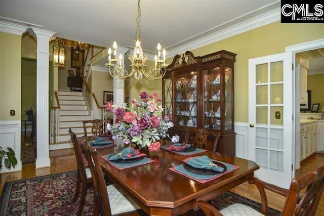 dining space with a wainscoted wall, ornate columns, an inviting chandelier, and crown molding