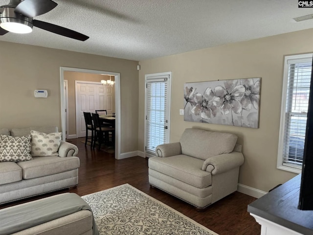 living area with a textured ceiling, dark wood-type flooring, ceiling fan with notable chandelier, and baseboards